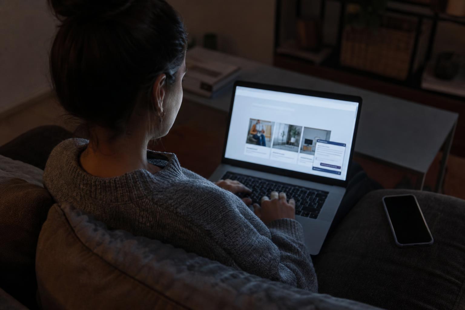 A person on a couch at night, lit by a laptop screen, typing a question into a website chat widget