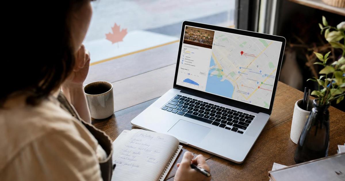 A small business owner in a Canadian storefront reviewing their Google Business Profile listing on a laptop at a sunlit desk