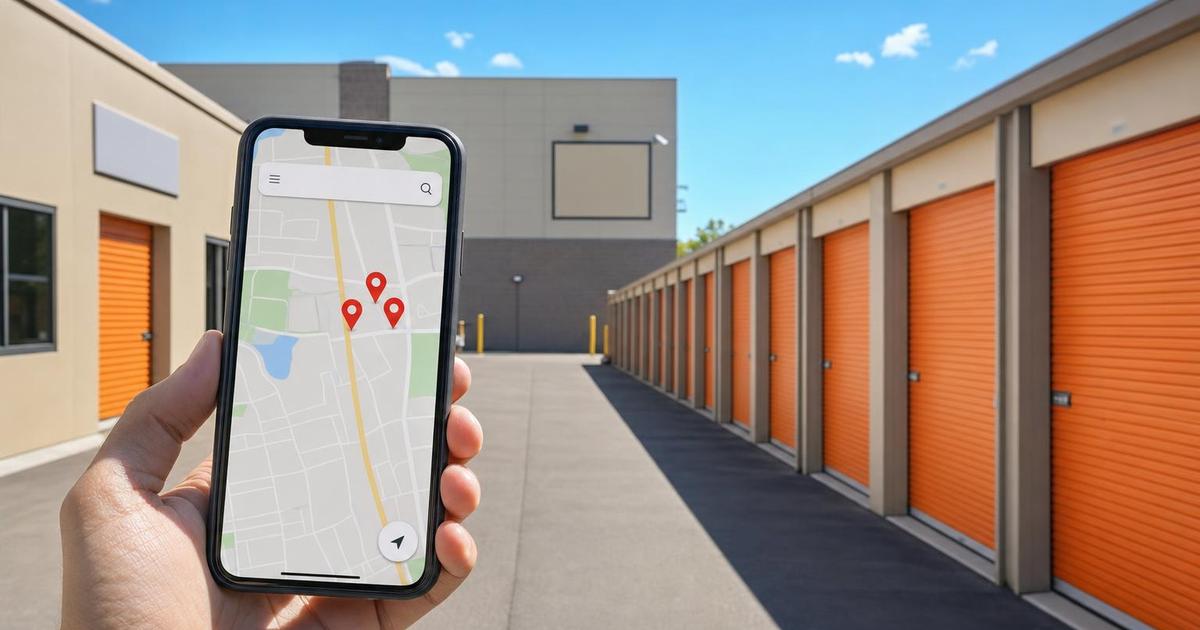 A hand holding a smartphone showing a generic map with three clustered location pins, in front of a row of self-storage units with orange roll-up doors