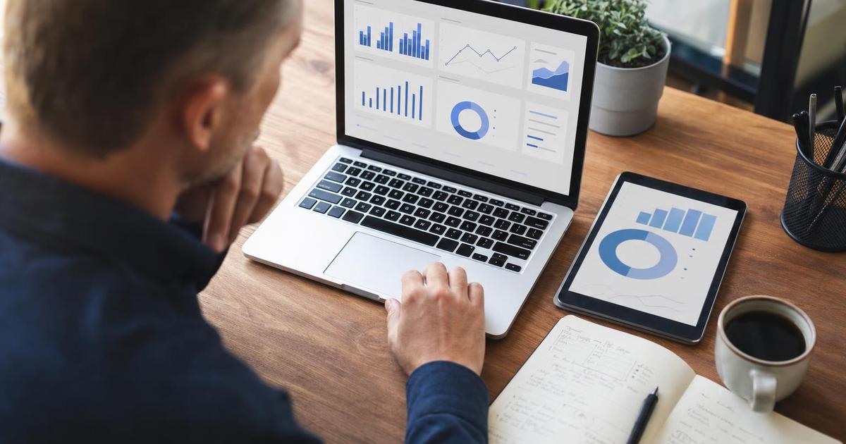 A small business owner reviewing a marketing operations dashboard with charts and graphs on a laptop and tablet at a tidy desk