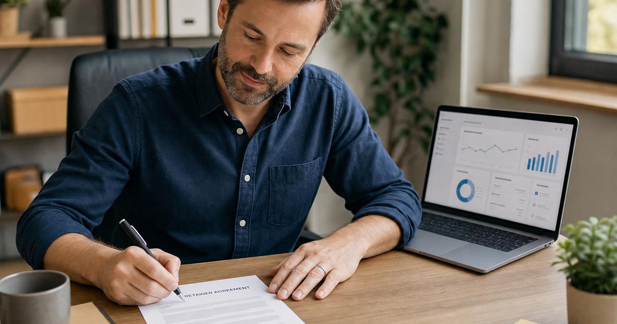 A small business owner reviewing and signing a marketing retainer agreement at a desk, a laptop showing a simple dashboard nearby