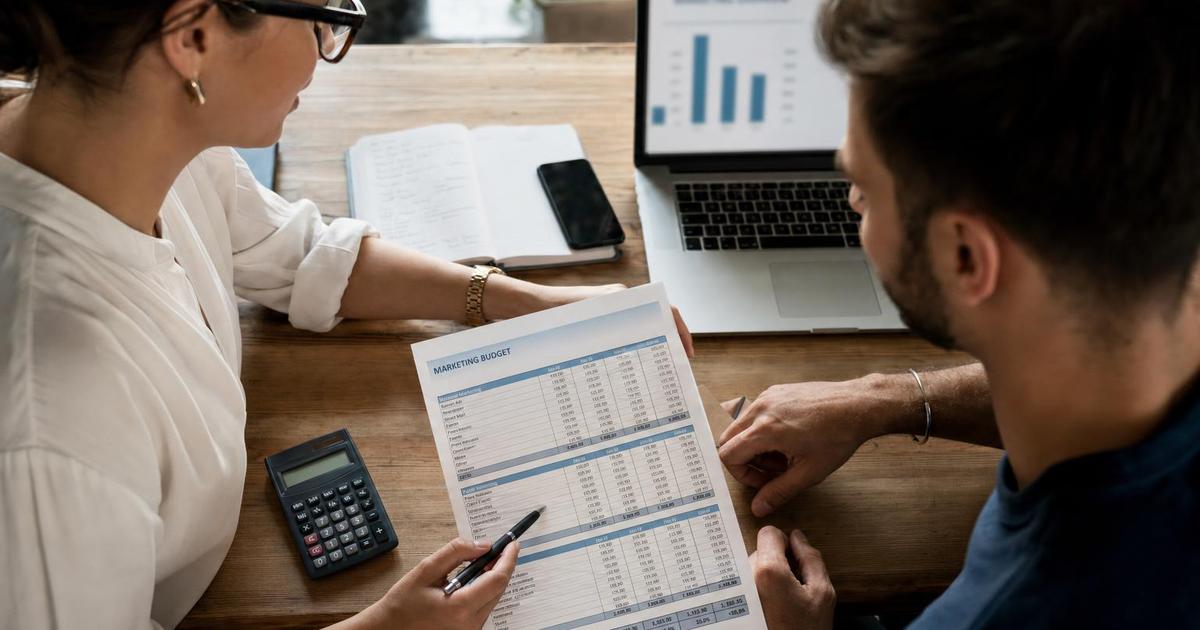 Two small business colleagues reviewing marketing budget numbers with a calculator and laptop